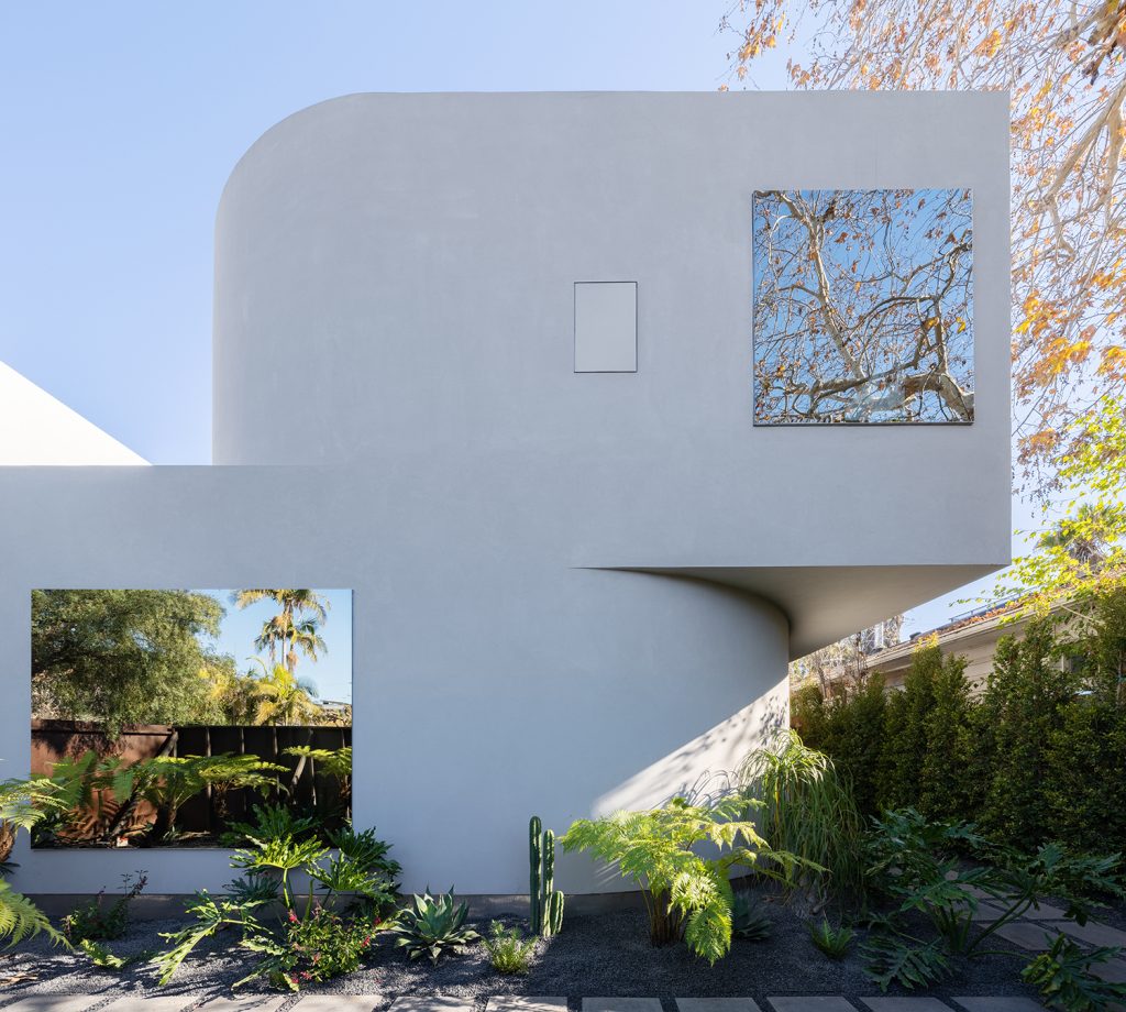 Radius House – Zaobljena bela fasada ob zelenju.