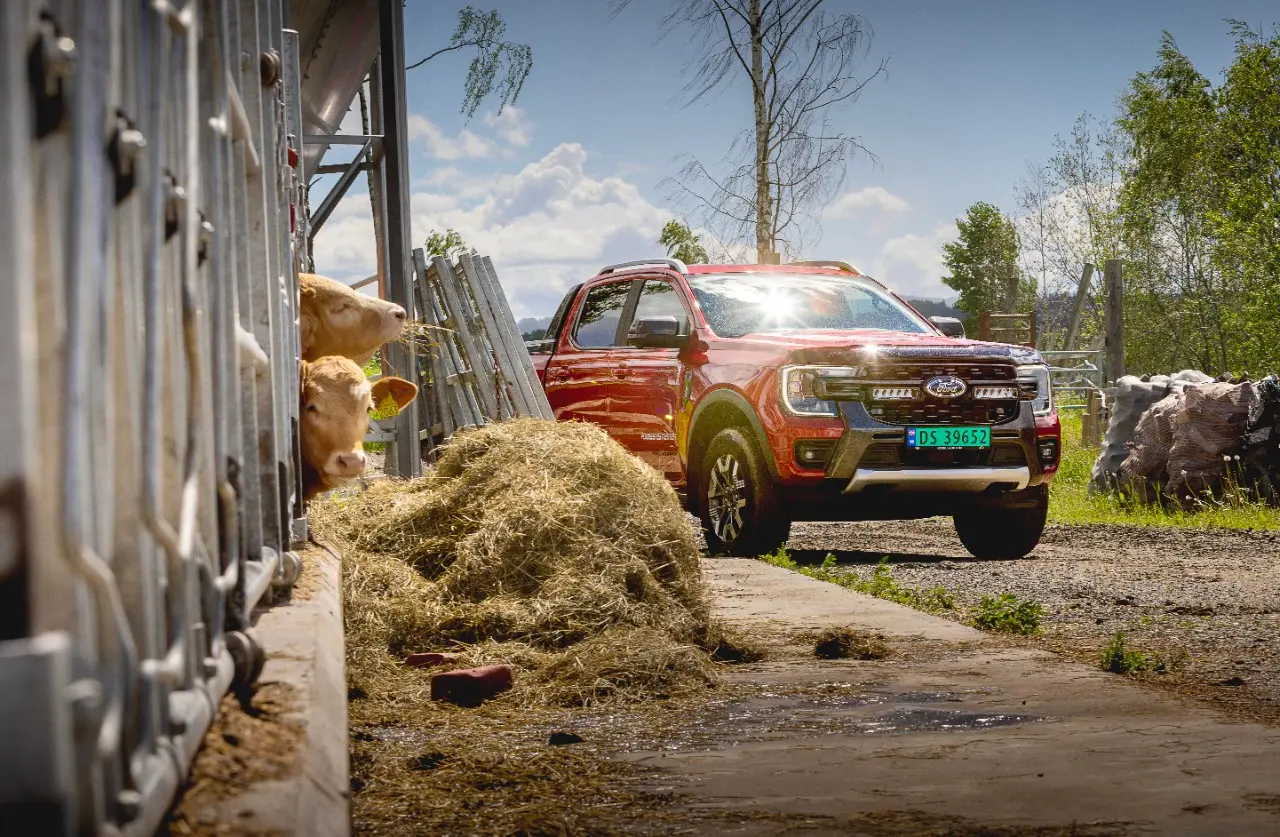 Rdeč pickup na dvorišču kmetije ob hlevu in kupu sena.